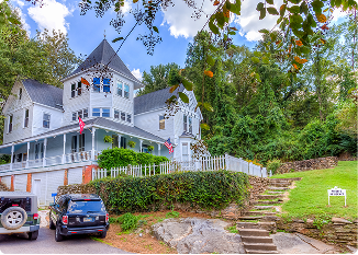 Victorian house with turret and porch in Central Alabama with lush greenery.