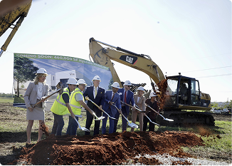 Group of professionals at groundbreaking ceremony with excavator in Central Alabama.