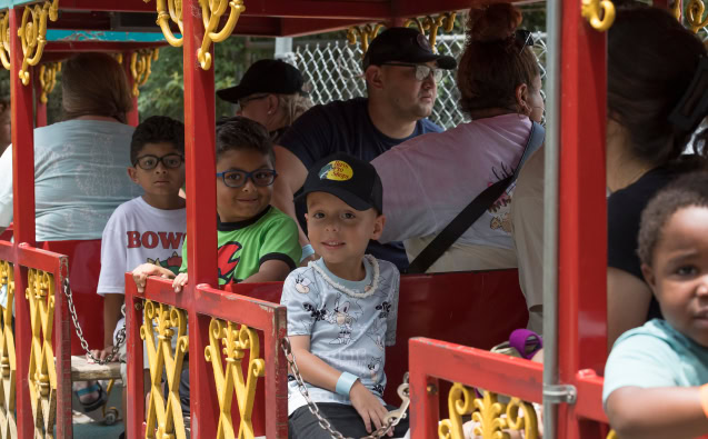 Family riding a colorful amusement park train with children and adults.
