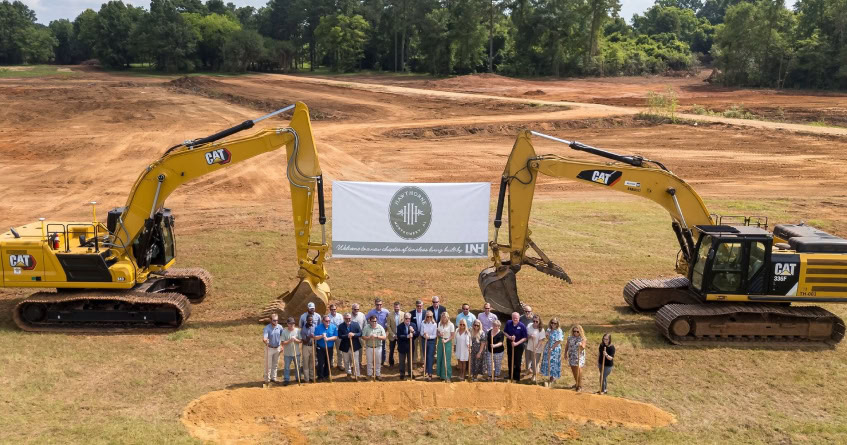 Group of people at groundbreaking ceremony with excavators in Central Alabama.