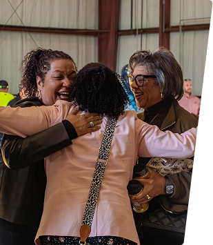 Group of diverse women embracing and smiling at a community event in Alabama.